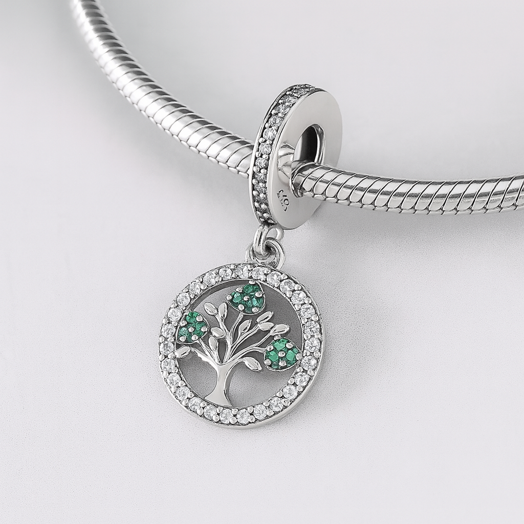 Silver charm with tree design and green stones on a white background