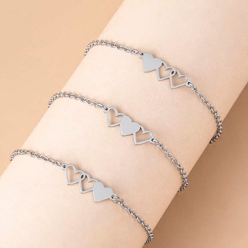 Silver heart-shaped bracelet on a wrist against a beige background