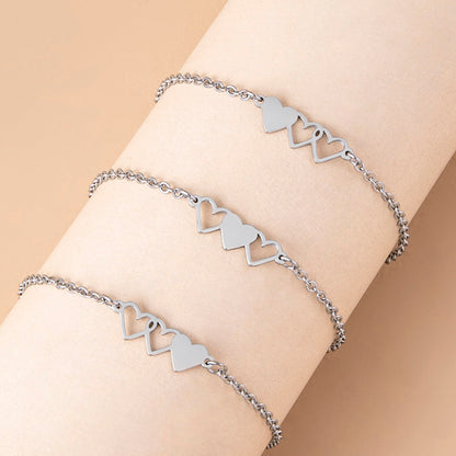 Silver heart-shaped bracelet on a wrist against a beige background
