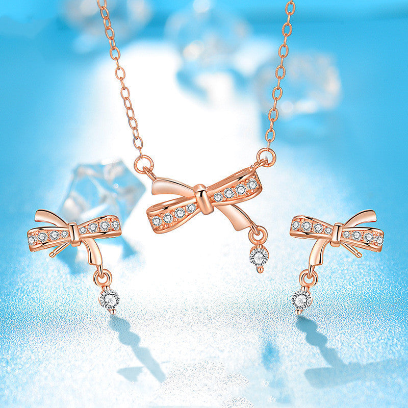 Rose gold bow-shaped jewelry set with diamond accents on a light blue background